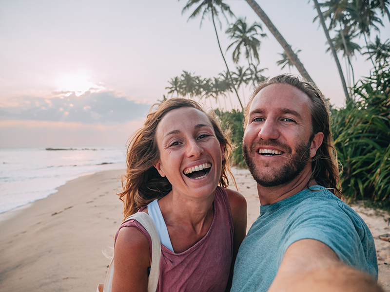 Young couple taking mobile phone selfie on tropical beach at sunset